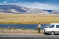 The driver of a tourist minibus parked on the side of the road looks at a tourist campsite on the lake