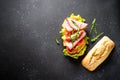 Ciabatta sandwich with lettuce, cheese, tomatoes and ham on black table. Royalty Free Stock Photo