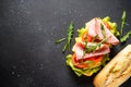 Ciabatta sandwich with lettuce, cheese, tomatoes and ham on black table. Royalty Free Stock Photo