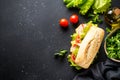 Ciabatta sandwich with lettuce, cheese, tomatoes and ham on black table. Royalty Free Stock Photo