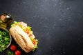 Ciabatta sandwich with lettuce, cheese, tomatoes and ham on black table. Royalty Free Stock Photo