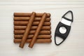 Cigars and guillotine cutter on white wooden table, flat lay