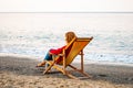 Woman resting sitting on wooden deckchair on sand beach on Tyrrhenian sea in Village Camping Odyssey in Italy