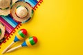 Top view photo of sombrero hats colorful striped serape and couple of maracas on isolated vivid yellow background