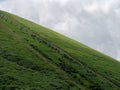 Cinder cone mountain covered with green annual plant against clouds background