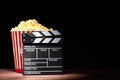 Cinema concept. Popcorn in a box and movie clapper on wooden table under beam of light against black background Royalty Free Stock Photo