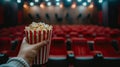 cinema with a hand holding popcorn in front of a movie screen, while the blurred cinema hall in the background sets the