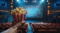 cinema with a hand holding popcorn in front of a movie screen, while the blurred cinema hall in the background sets the