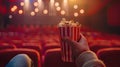 cinema with a hand holding popcorn in front of a movie screen, while the blurred cinema hall in the background sets the