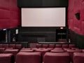 Cinema - interior of a movie theatre with empty red and black seats with white screen Royalty Free Stock Photo