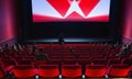 Cinema wide screen and people in red chairs in the cinema hall. Blurred People silhouettes watching movie performance