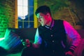 Cinematic portrait of handsome young man using devices, gadgets in neon lighted interior. Youth culture, bright colors
