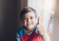 Cinematic portrait Happy young boy looking up to camera with smiling face, Positive Kid sitting next to window in living room Royalty Free Stock Photo