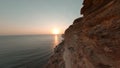 Cinematic shot from fpv drone. Golden sunset in sea and cliffy coast above. Rocky coastline on evening sunset aerial landscape. Mo