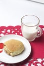 A cinnamon roll lies on a plate. Nearby is a glass of milk. All this on a red openwork napkin. Royalty Free Stock Photo