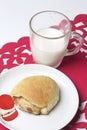 A cinnamon roll lies on a plate. Nearby is a glass of milk. All this on a red openwork napkin. Royalty Free Stock Photo