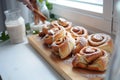 cinnamon rolls on wooden board, person with glass milk, ivy on window ledge Royalty Free Stock Photo