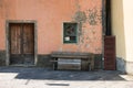 Building exterior in a state of disrepair. Facade with peeling paint, worn wooden double doors, and an old wood bench.