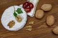 A circle of camembert cheese with white noble mold lies on a wooden board. A piece of cheese with walnuts and grapes Royalty Free Stock Photo