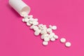 Circle pills tablets spilling out of a white plastic medicine bottle on pink background Royalty Free Stock Photo