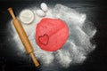 Circle of red dough with heart-shape cut-out. Black table sprinkled with flour, rolling pin and eggs Royalty Free Stock Photo