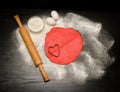 Circle of red dough with heart-shape cut-out. Black table sprinkled with flour, rolling pin and eggs. Royalty Free Stock Photo