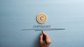 Circled letter C on a wooden cut circle with male hand writing a Copyright word under it