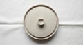 A circular, beige ceramic pot lid with a central handle is placed on a white cloth surface. The Royalty Free Stock Photo