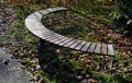 Circular bench in the shape of an arch with wood paneling with brown wooden planks. Yellow leaves lie on a seating area in an autu