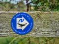 A circular, blue and white sign fixed to a wooden stile points the way of St Oswald`s Way and the Northumberland Coast Path