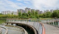 Circular plank-paved footbridge over lake before multi-story apartments in sunny summer