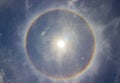 Circular rainbow halo around the sun among blue sky and white clouds Royalty Free Stock Photo