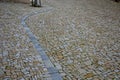 Circular tree bowls in rough irregularly stacked paving. The brown walls of a historic building with a longitudinal canal distract