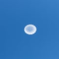 A circular white cloud formation is centered against a clear blue sky. The cloud has a Royalty Free Stock Photo