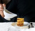 A circumcised man in a black T-shirt holds a white gravy boat in his hands and pours the curd cheesecakes on a plain Royalty Free Stock Photo