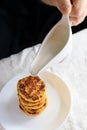 A circumcised man in a black T-shirt holds a white gravy boat in his hands and pours the curd cheesecakes on a plain Royalty Free Stock Photo