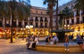 Citizens and tourists stroll and relax in cafe in light of streetlight on Royal square in Barcelona.