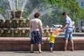 Citizens on a walk in the city park near the fountain. A young man returns a balloon to a little boy