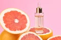 Citrus essential oil in bottle with fresh grapefruit halves on pink background. Royalty Free Stock Photo