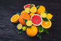 Citrus fruits, half grapefruits, lemons, oranges, limes with green leaves lie on a brown wooden table