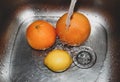 Citrus fruits lie in the sink under running water, before washing. Lemon, orange and grapefruit