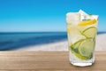 Citrus lemonade with ice cubes on table at beach, space for text