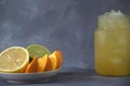 A citrus platter of lemon, orange and lime slices on a saucer and a glass mug with citrus juice and ice stand nearby. Close-up Royalty Free Stock Photo