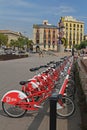 City bicycles stand in a row on a parking for rent against the background of the sculpture `Barcelona head` on the waterfront at t