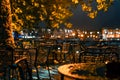 City cafe terrace near the river in the rainy autumn evening in the lantern light. Raindrops on outdoor metal furniture Royalty Free Stock Photo