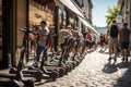 In the city, electric scooters stand in a line along a cobblestone road, with distant pedestrians