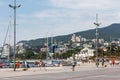 City embankment along the sea coast, with moored yachts and tourists. Mountains in the background