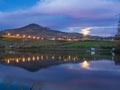 City lights, rising moon and mountain reflected in pond