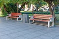 City park or street with green trees and tile - two neat benches made of concrete and wood, between the rubbish bin.