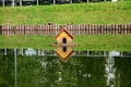 A city pond with a duck house, a steep bank with wooden piles and their beautiful reflections in the water on a clear sunny day.